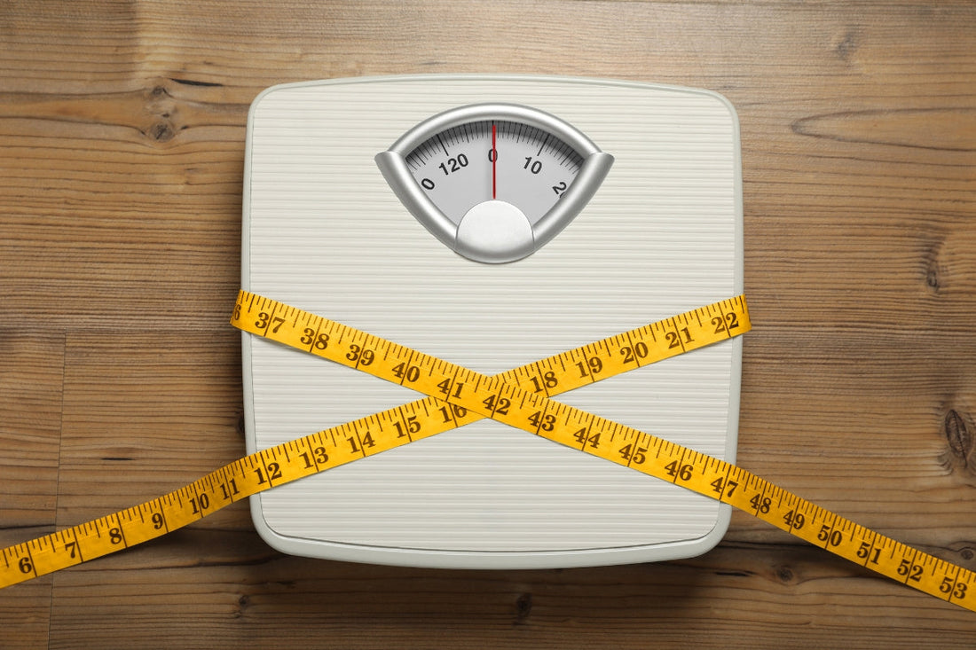 Scales tied with measuring tape on wooden background, top view