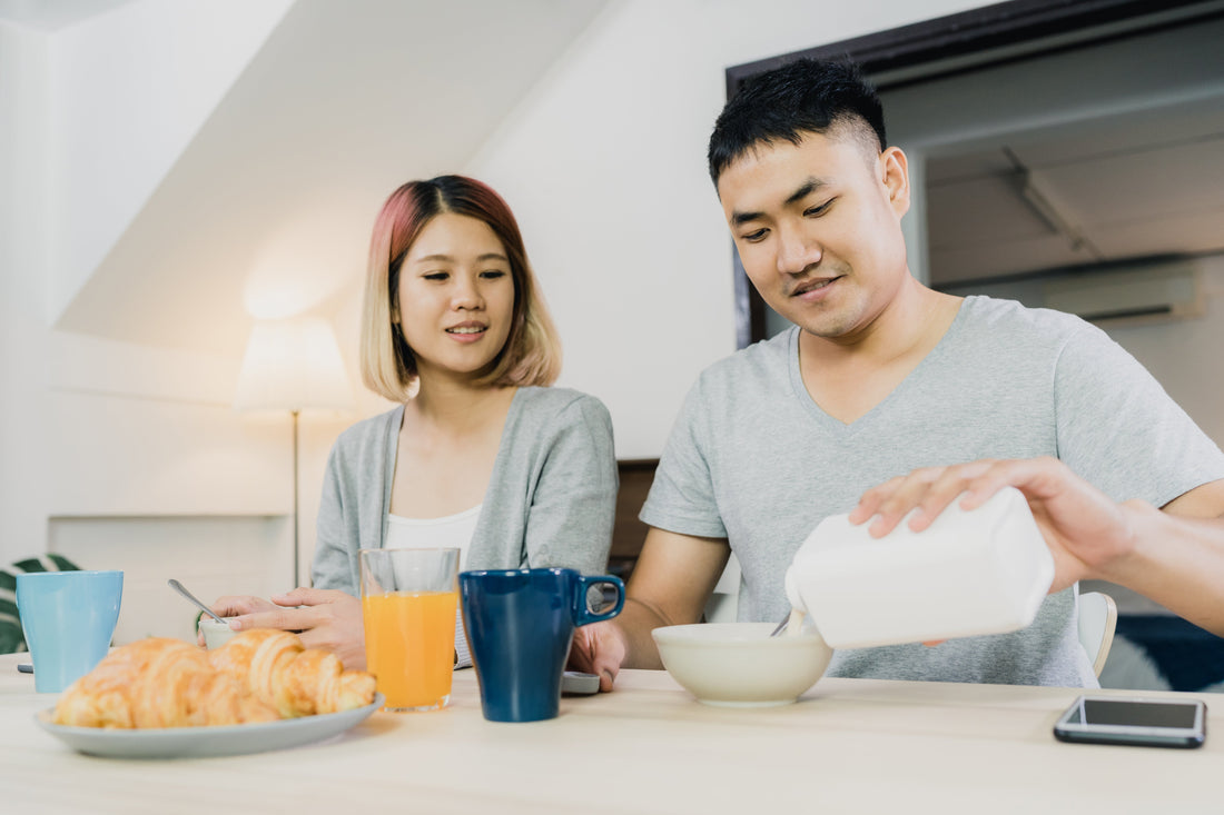 Couple enjoying cereal for breakfast at home with croissants, orange juice and coffee on the table.